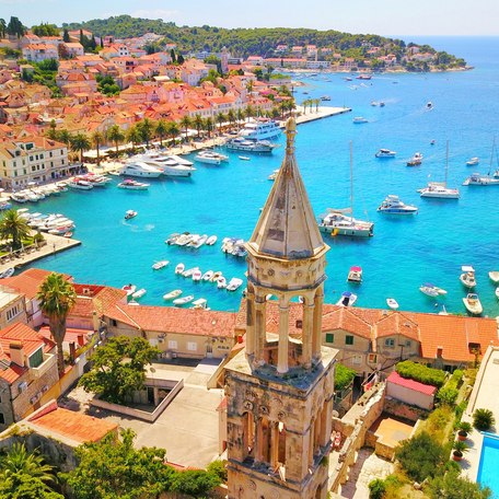 Overview of rooftops and a steeple in Croatia, leading down to an azure watered marina
