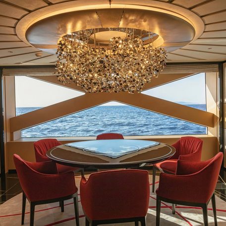 Overview of a games table onboard charter yacht PROJECT X with a chandelier overhead and a large window in the background