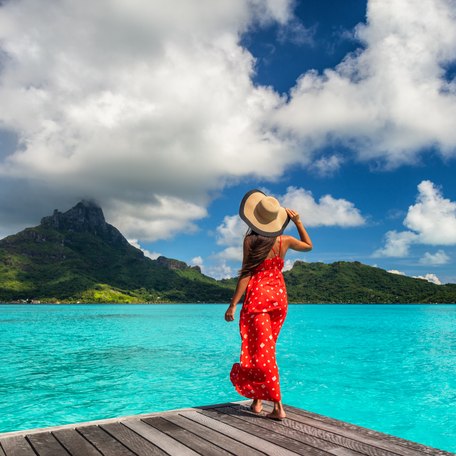 Female charter guest in a red dress stands on pontoon overlooking French Polynesia islands