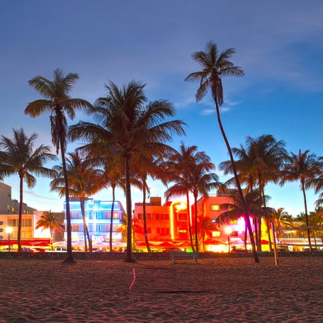 Overview from the beach looking at Downtown Miami at night, with buildings lit in different colors.