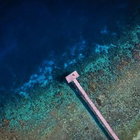 Aerial shot of a pier extending into bright blue water 