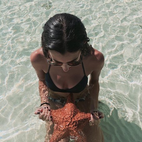 Girl in bikini kneeling in shallow water with a starfish on her lap