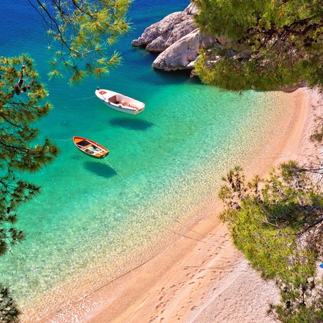 Aerial view looking down on a deserted sandy beach with two small tenders in the bay