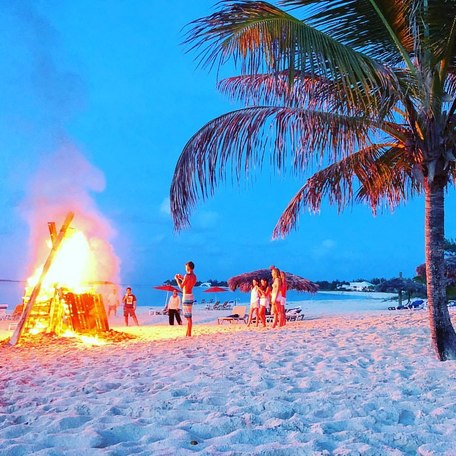 Group of people gathered round a beach bonfire at sundown 