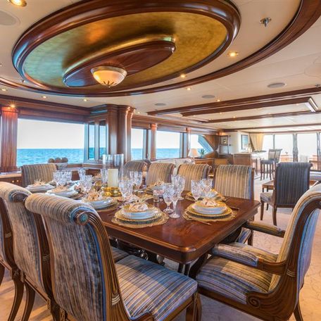 Overview of the interior dining area onboard charter yacht MISS STEPHANIE, long 10-seater table surrounded by windows.
