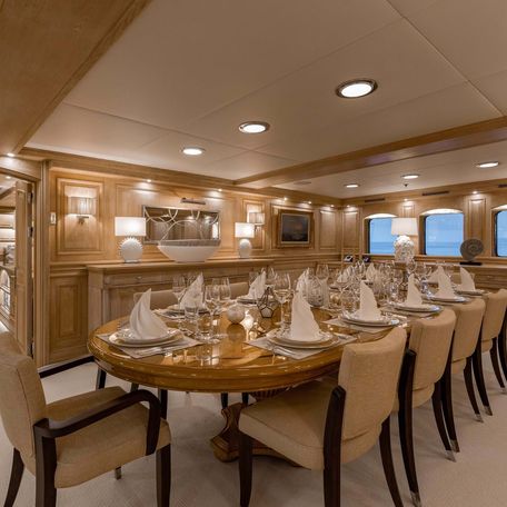 Dining area onboard charter yacht NERO, central dining table for up to 12 charter guests with small windows in background