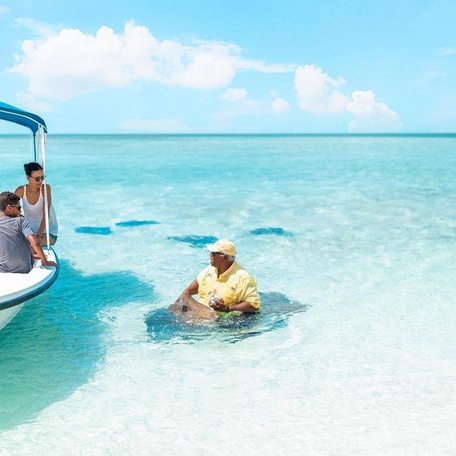 Family in a boat watching a man sitting with sting rays in the water 