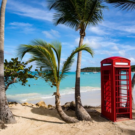 A red phone box standing on a sandy beach with palm trees in the British Virgin Islands
