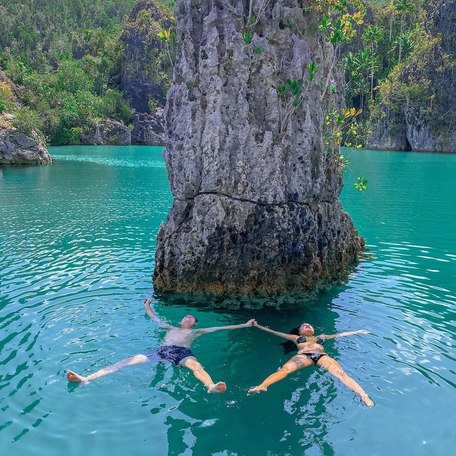 Two people making star shapes in the lagoon's water in front of a karst