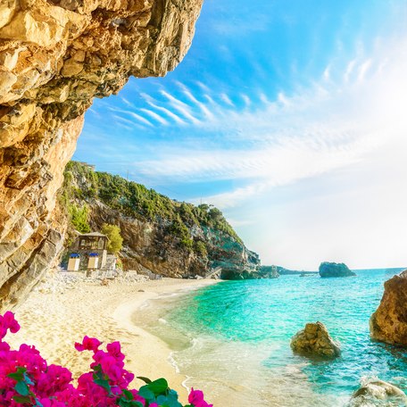 A secluded cavern on a quiet beach in Greece, with pink flowers in the foreground