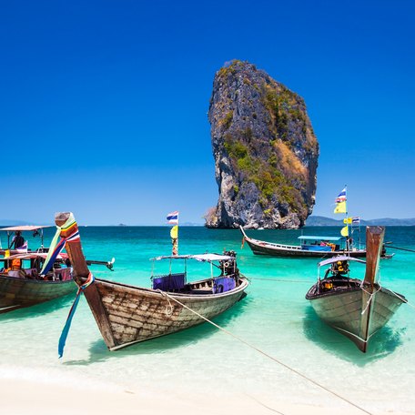 A beach in Phuket, with a large rock in the sea and small boats on the sand.