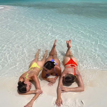 3 girls wearing colorful bikinis lying in the water by the shore