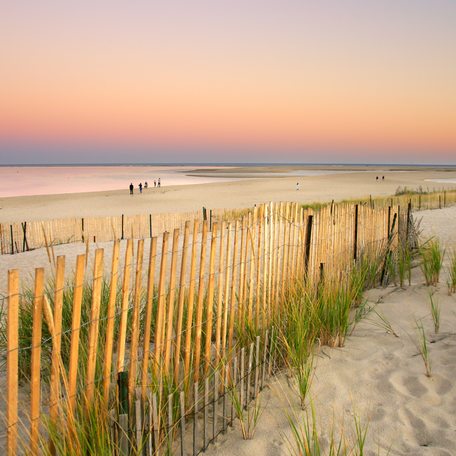 Picket fence leading down to a sandy beach at sunset