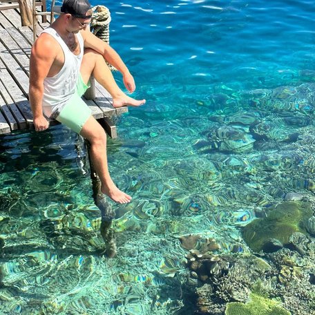 Man sitting on a jetty looking down over the coral in clear blue water