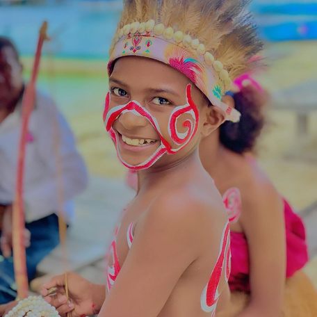 Child with red body paint and traditional dress smiling 