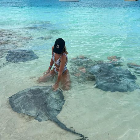 Woman in bikini kneeling in the clear water petting stingrays 
