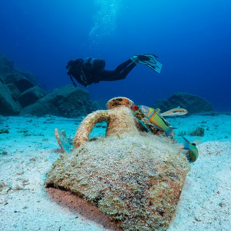 A charter guest diving in Greece with a large submerged vase in the foreground