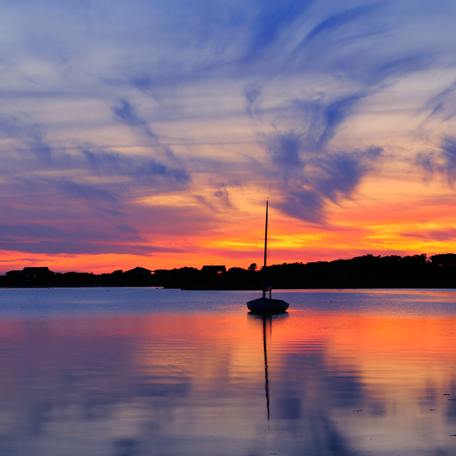 A single sailing yacht charter sat on still waters at sunset