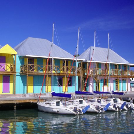 A line of colored houses in Antigua with a pontoon outside and five small boats.