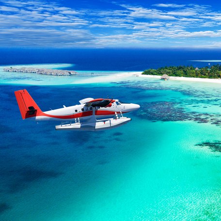 A red and white seaplane flying over the Maldives