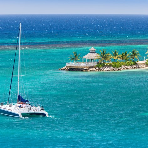 Sailboat on turquoise sea and beautiful beach with palm trees in the background