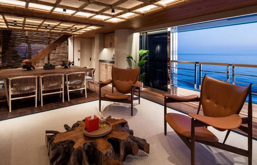 Interiors onboard private yacht charter KING BENJI, seating area in the foreground with dining area and exterior deck visible in the background