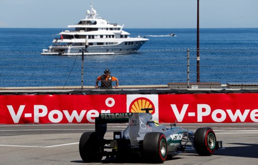 A formula 1 car on the Monaco Grand Prix race track with a superyacht anchored in the distance