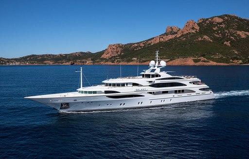 Overview of charter yacht GALAXY underway with elevated terrain in the background.