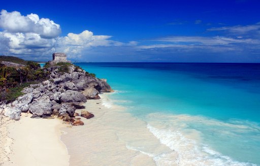 Mexican coast, with white sand beach, azure ocean and Mayan ruins on cliff