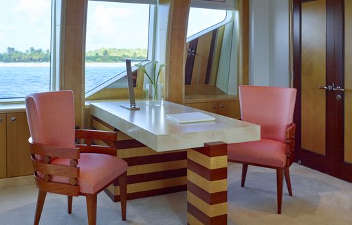 Table and chair onboard Victoria Del Mar with plant on table and windows looking out to sea