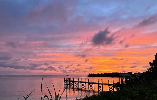 Sky illuminated pink and orange at sunset over the Cay with reeds and jetties silhouetted