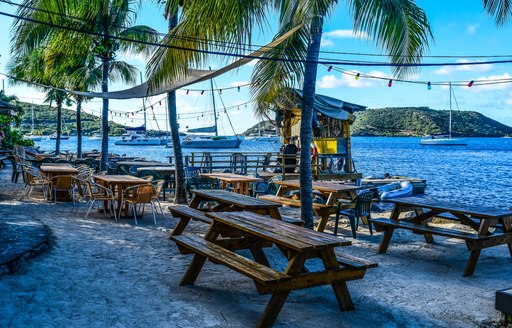 Tables and chairs of a restaurant on the beach in the Virgin Islands, with palm trees and sea in the background