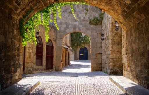 cobbled stone street in greece with ivy hanging over door archway