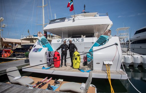 Charter yacht SEA AXIS at the Newport Charter Yacht Show, with two crew members posing with a collection of water toys