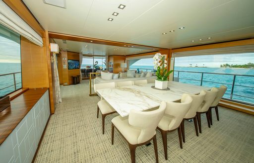 Interior dining table and surrounding seats with large adjacent window onboard luxury yacht charter REHAB