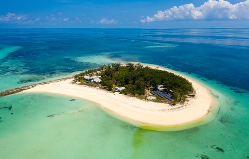 aerial view of thanda island with shallow green and blue seas and white sandy beaches, with plants covering interior of island. solar panels visible also