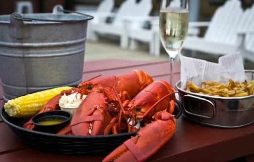 A wooden table set with a classic New England lobster dish with a glass of champagne