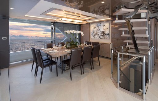 Overview of the interior dining area onboard charter yacht ENTREPRENEUR, surrounded by full height windows and a staircase to starboard