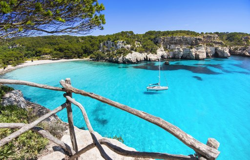 Lone sailing yacht sits in a turquoise lagoon with beach and forest