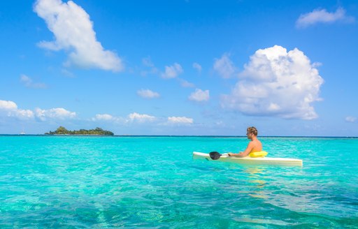 Man in kayak in clear water with small island in distance