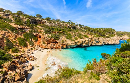 View of beach on Majorca, with rocky coastline behind and clear water at fringe of beach