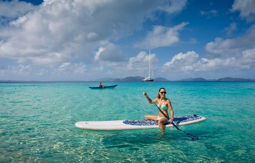 charter guest on paddle board with superyacht MARAE in background