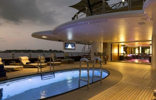 Swimming pool and sun loungers on exterior deck of yacht charter NIRVANA. Glimpse of interior main deck visible in background.