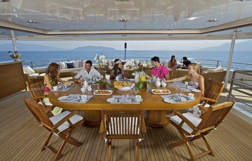 Geusts enjoying food onboard O'MEGA superyacht viewed from top at wooden table on deck under cover