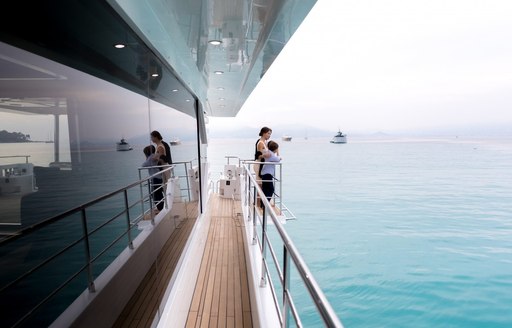 guests look out over the balcony on the sidedeck of motor yacht ONEWORLD