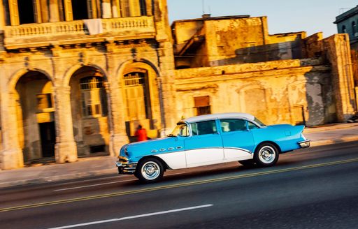 A classic 1950s car cruises down Cuban street lined with colonial buildings