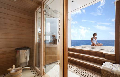 A charter guest sits cross-legged on a foldout balcony attached to a superyacht