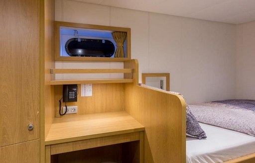 View of bedroom in Game Changer yacht, bed and wooden desk visible