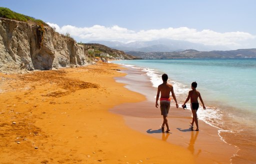 People walking along a secluded red sand beach in Greece