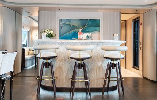 An interior wet bar and three stools with a painting aft onboard charter yacht M